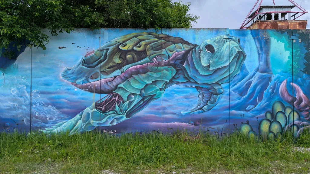 Mural of a stylized, biomechanical sea turtle swimming underwater, painted on a metal wall