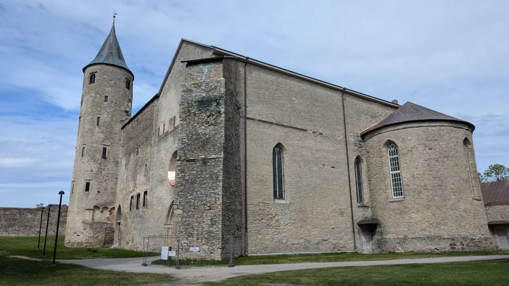 Medieval stone castle with a tall round tower and a semi-circular chapel under a blue sky