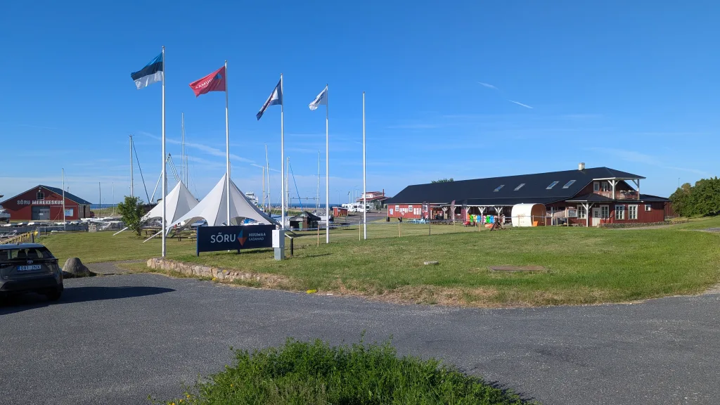 Sõru harbor in Hiiumaa, Estonia, featuring red maritime buildings, flags, and white tents under a clear blue sky