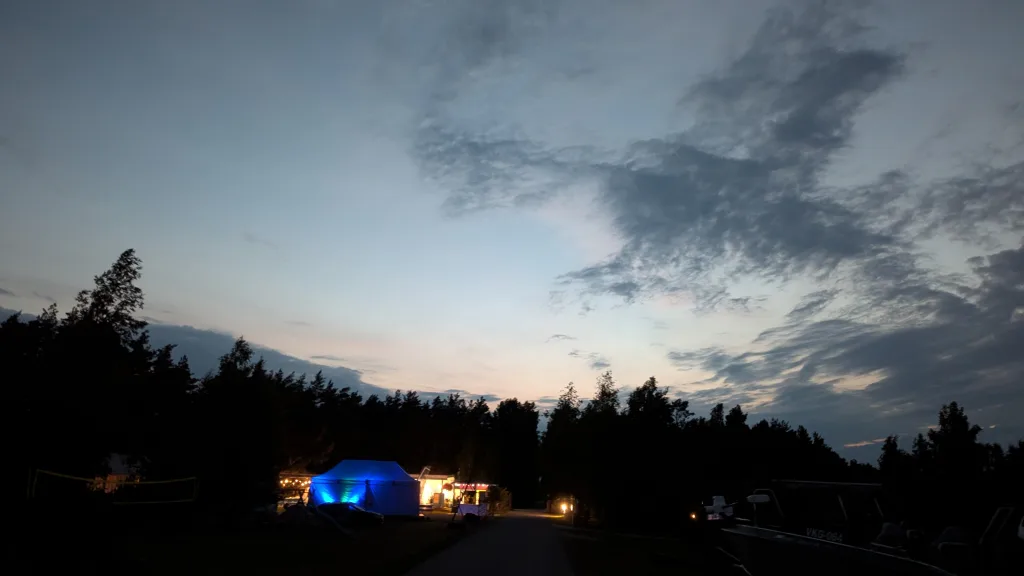 Glowing blue tent at a campsite at twilight, silhouetted by trees under a cloudy sky