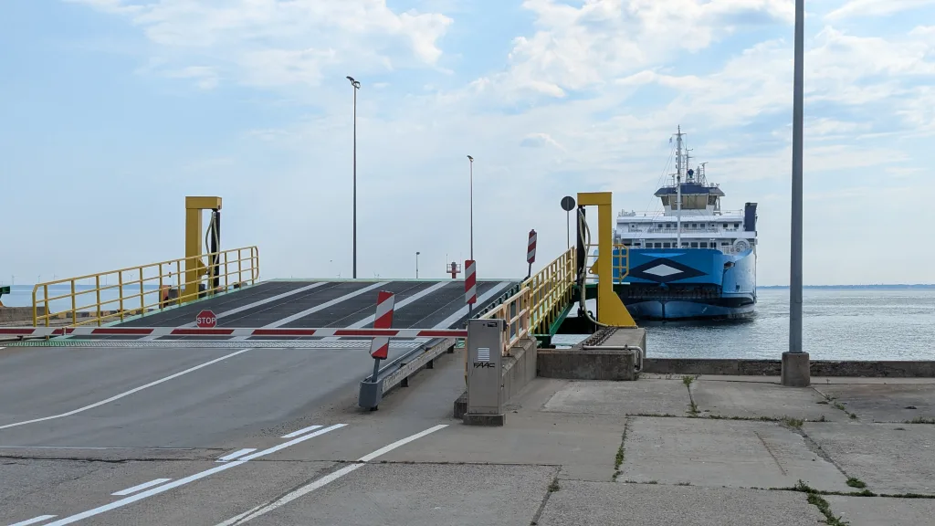 A blue and white ferry ship approaching a closed loading ramp at a harbor