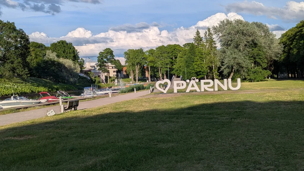 Large white I heart Pärnu sign in a grassy park next to a river with docked boats