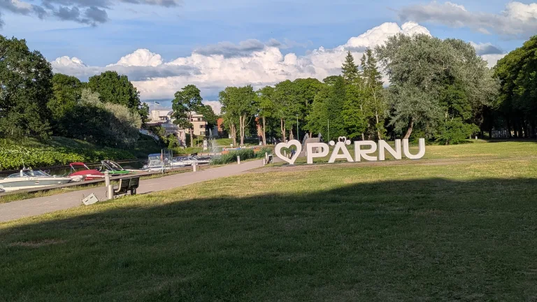Large white I heart Pärnu sign in a grassy park next to a river with docked boats